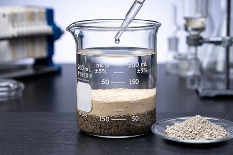 FlocClay bench test beaker with clear water, settled flocs, and powdered treatment product